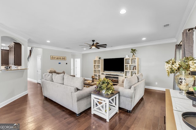 living area featuring visible vents, arched walkways, a glass covered fireplace, dark wood-style floors, and crown molding