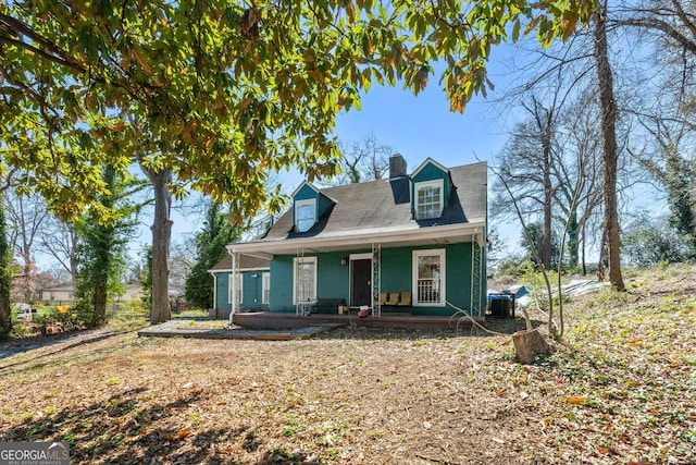 cape cod home with covered porch, a chimney, and central AC