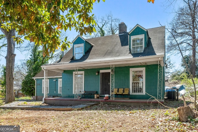 new england style home with covered porch, central AC, a chimney, and roof with shingles