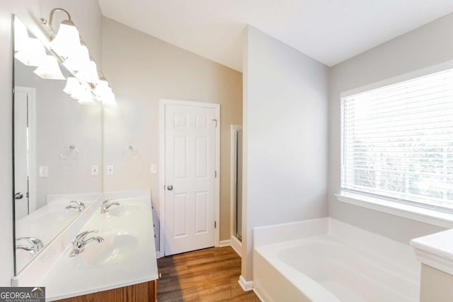 full bath featuring a garden tub, wood finished floors, a sink, double vanity, and a stall shower