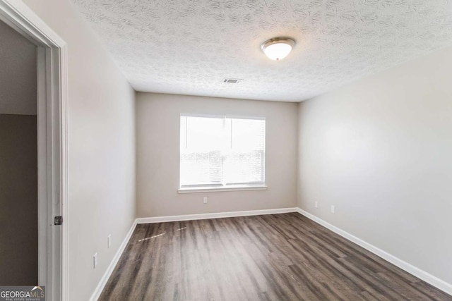 unfurnished room with dark wood-style flooring, visible vents, a textured ceiling, and baseboards