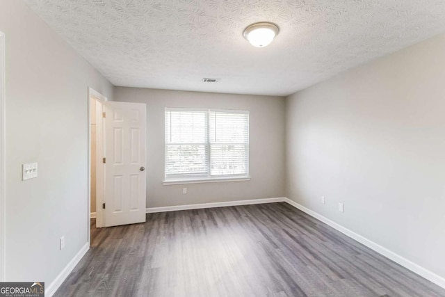 spare room featuring visible vents, a textured ceiling, baseboards, and wood finished floors