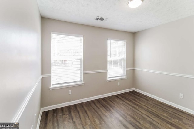 empty room with a textured ceiling, wood finished floors, visible vents, and baseboards