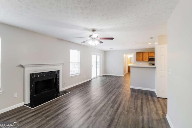 unfurnished living room featuring a ceiling fan, dark wood-style flooring, a high end fireplace, and baseboards