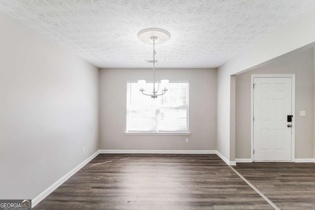 unfurnished dining area featuring dark wood-style floors, a chandelier, a textured ceiling, and baseboards