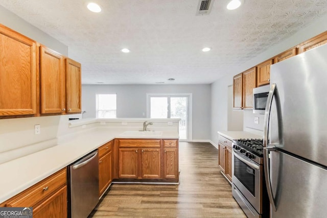 kitchen with visible vents, wood finished floors, a peninsula, stainless steel appliances, and a sink