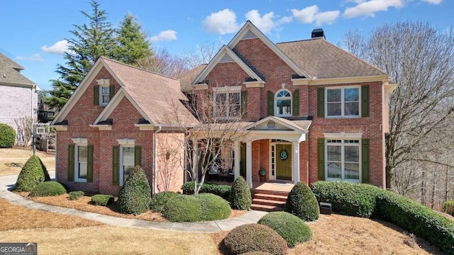 view of front of house featuring a porch, brick siding, a chimney, and a shingled roof