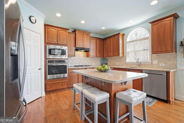 kitchen featuring stainless steel appliances, light wood-style floors, a sink, and a kitchen breakfast bar