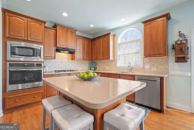 kitchen with appliances with stainless steel finishes, a kitchen breakfast bar, ornamental molding, under cabinet range hood, and a sink