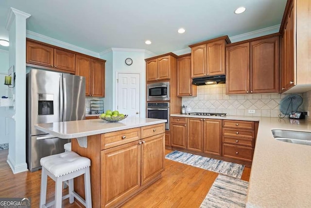 kitchen with a center island, a breakfast bar area, stainless steel appliances, light countertops, and under cabinet range hood