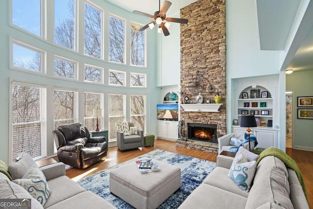 living room featuring built in shelves, a fireplace, a ceiling fan, and wood finished floors