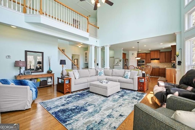 living area featuring light wood-style flooring, a high ceiling, a ceiling fan, stairs, and ornate columns