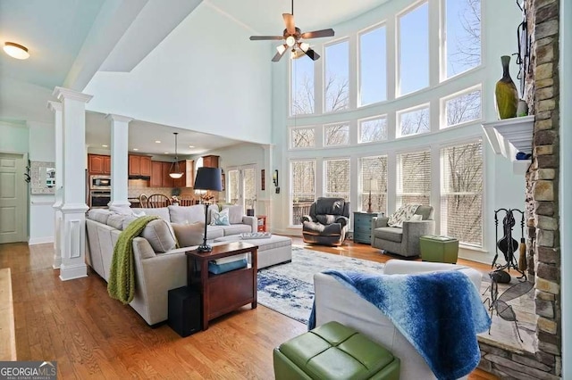 living area with ceiling fan, decorative columns, and light wood-style flooring