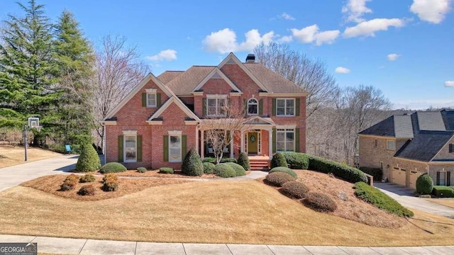 view of front facade with driveway, brick siding, and a chimney