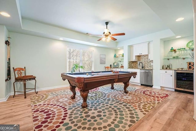 game room with wine cooler, a raised ceiling, wet bar, light wood-type flooring, and baseboards