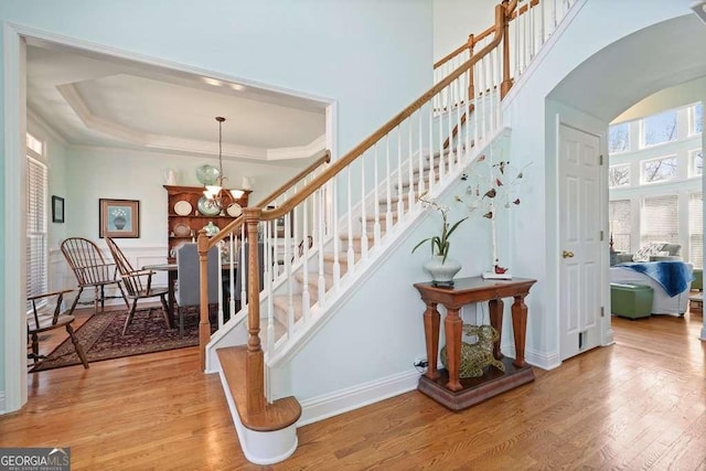 staircase featuring arched walkways, a raised ceiling, ornamental molding, wood finished floors, and a chandelier