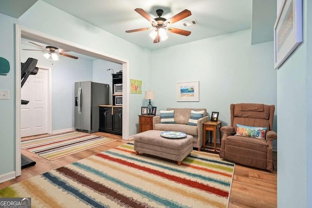 living area featuring light wood-style flooring, visible vents, ceiling fan, and baseboards