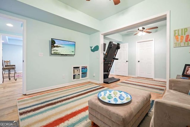 living room with light wood-type flooring, a ceiling fan, and baseboards