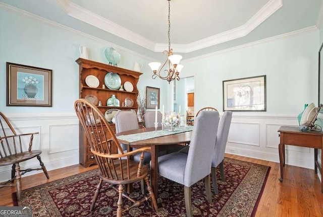 dining room featuring a wainscoted wall, crown molding, a decorative wall, an inviting chandelier, and wood finished floors