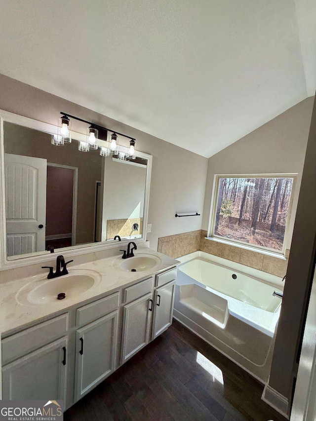 bathroom with wood finished floors, a sink, a bath, and double vanity