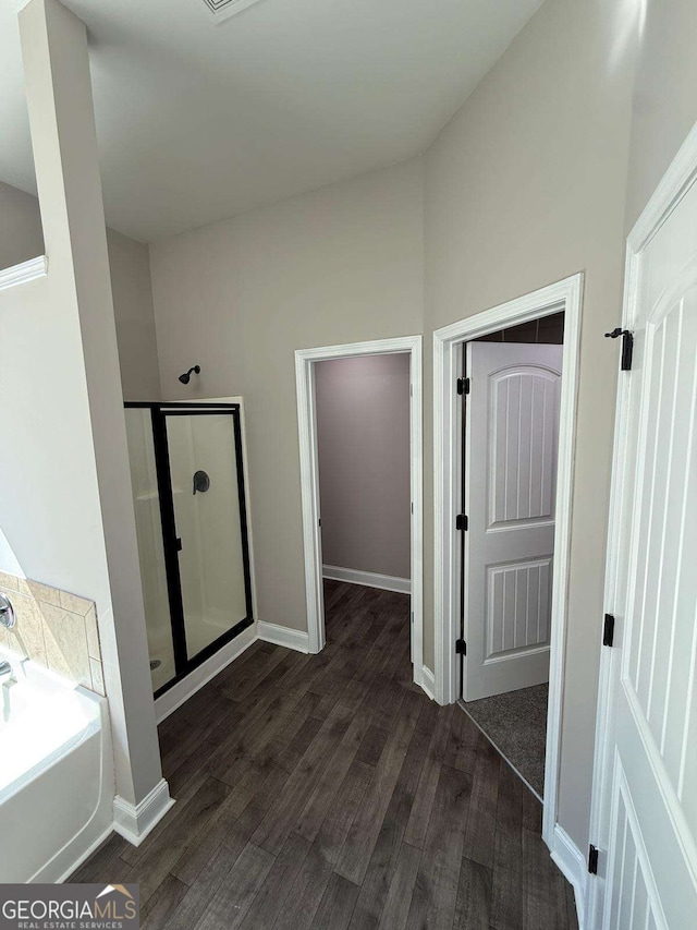 bathroom with a bath, a stall shower, baseboards, and wood finished floors