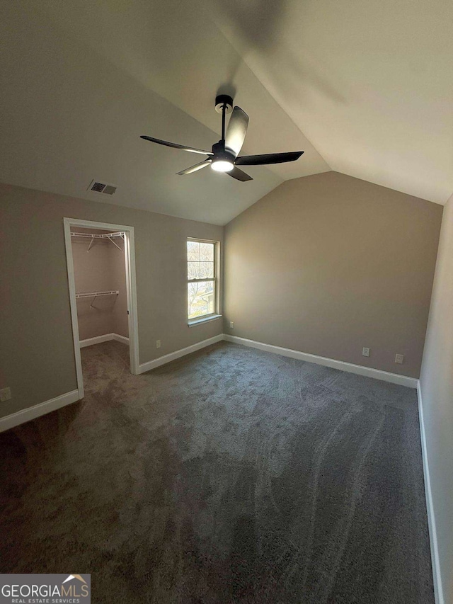 unfurnished bedroom featuring carpet, a walk in closet, visible vents, vaulted ceiling, and baseboards