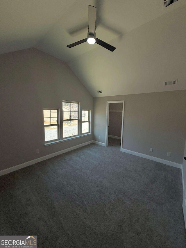 spare room with dark colored carpet, lofted ceiling, visible vents, a ceiling fan, and baseboards