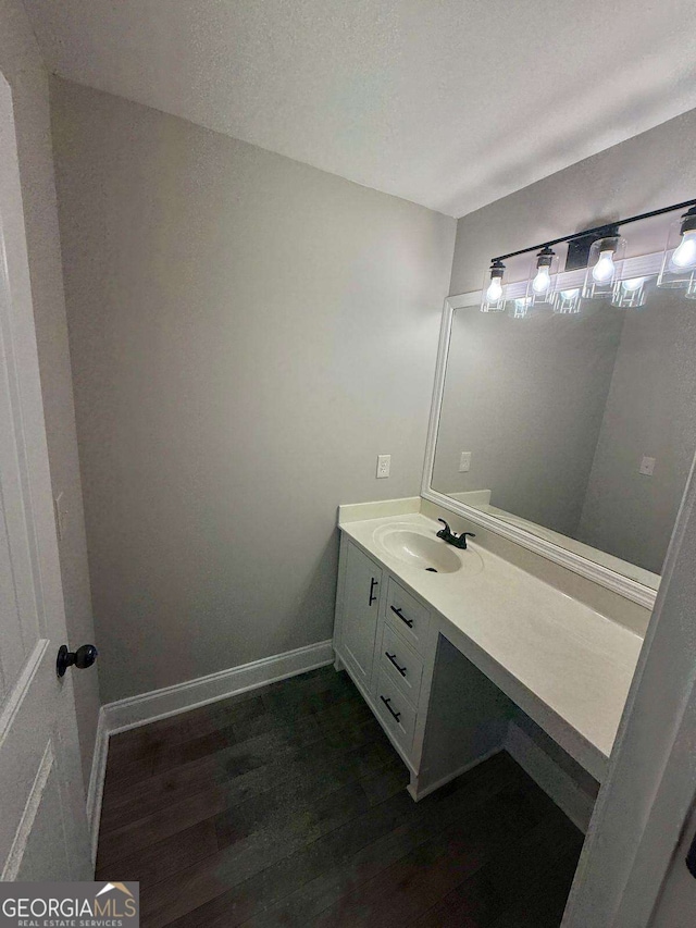 bathroom with a textured ceiling, baseboards, wood finished floors, and vanity