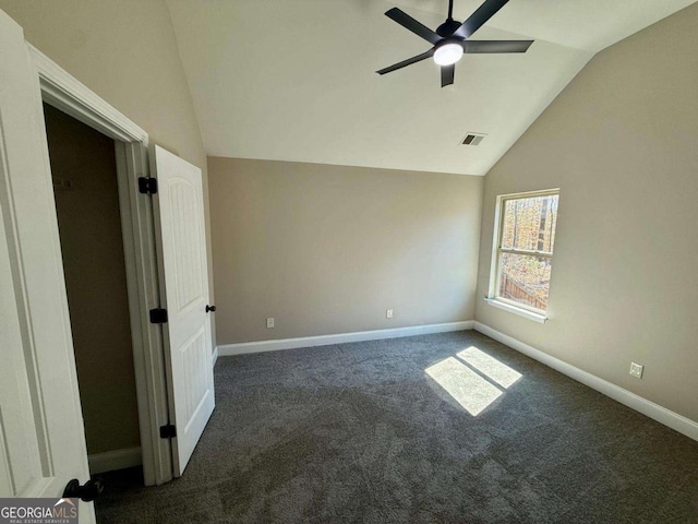 spare room with dark colored carpet, visible vents, vaulted ceiling, and baseboards