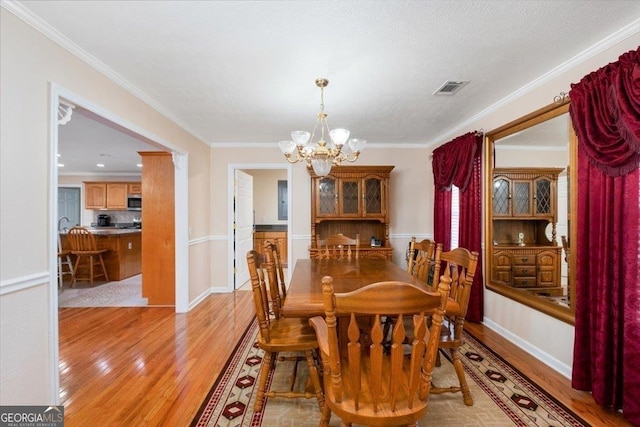 dining area featuring a chandelier, visible vents, ornamental molding, and light wood finished floors