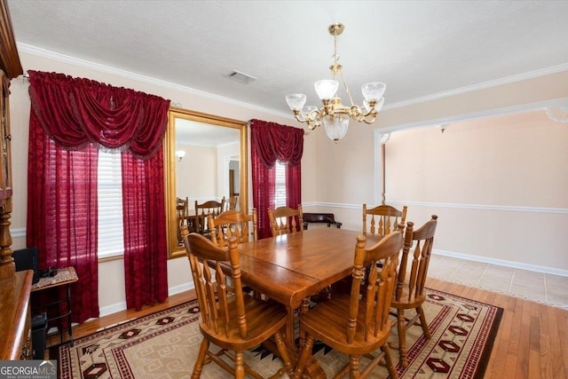 dining space featuring wood finished floors, visible vents, baseboards, an inviting chandelier, and crown molding