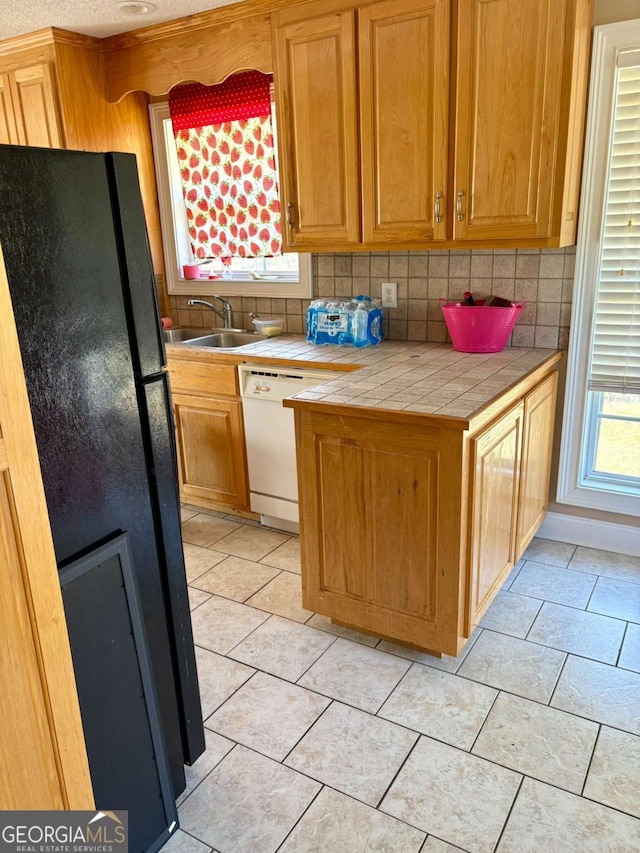 kitchen with tile counters, backsplash, freestanding refrigerator, white dishwasher, and a sink