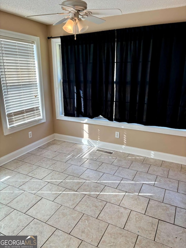 unfurnished room with a textured ceiling, light tile patterned floors, a ceiling fan, and baseboards