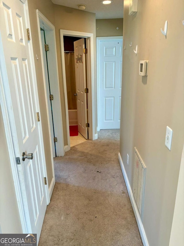 hallway with baseboards, visible vents, and carpet flooring