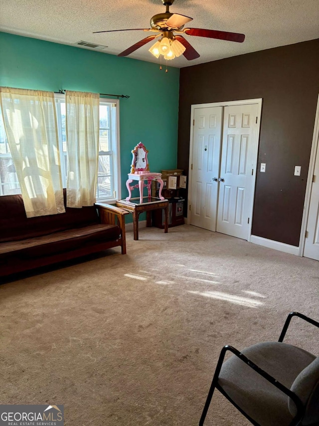 sitting room with visible vents, carpet flooring, ceiling fan, and a textured ceiling