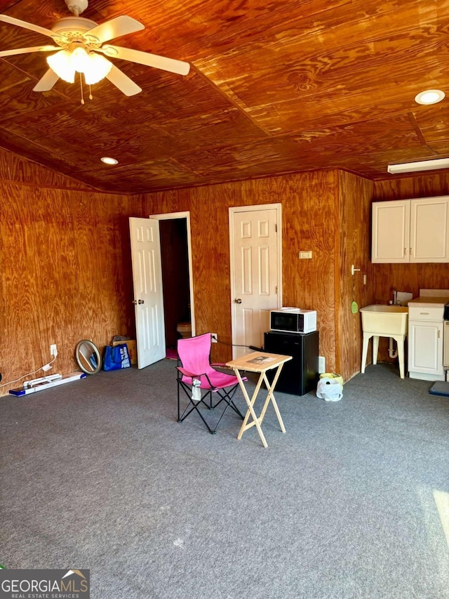 unfurnished room with wood walls, wood ceiling, ceiling fan, and carpet flooring