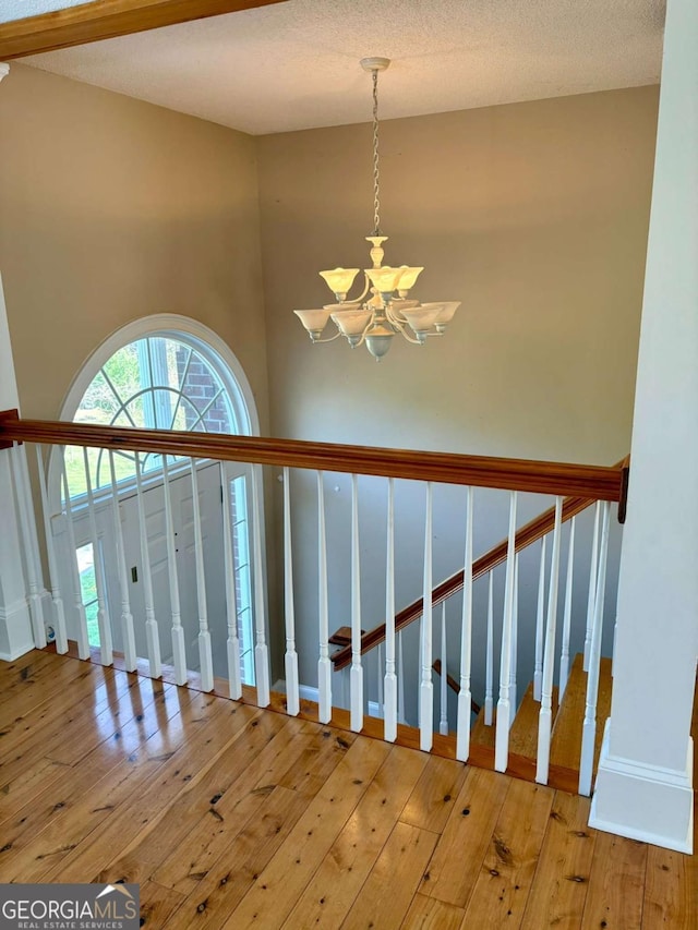 staircase featuring a chandelier, hardwood / wood-style floors, a textured ceiling, and baseboards