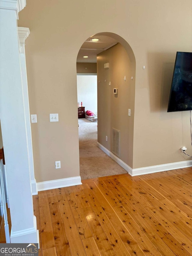 hallway with light wood-style floors, arched walkways, visible vents, and baseboards