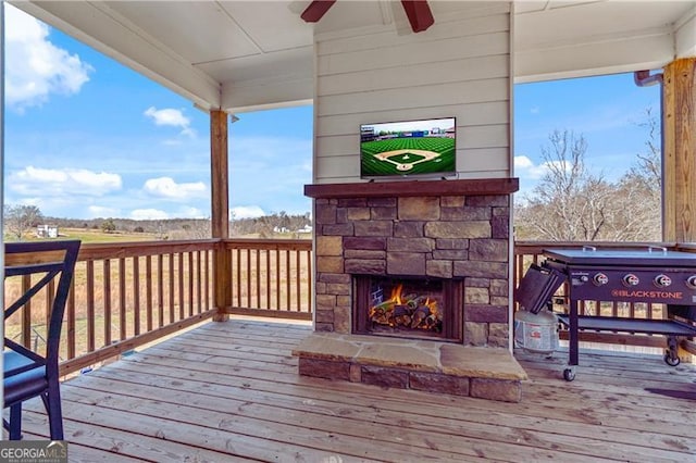 deck featuring ceiling fan and an outdoor stone fireplace