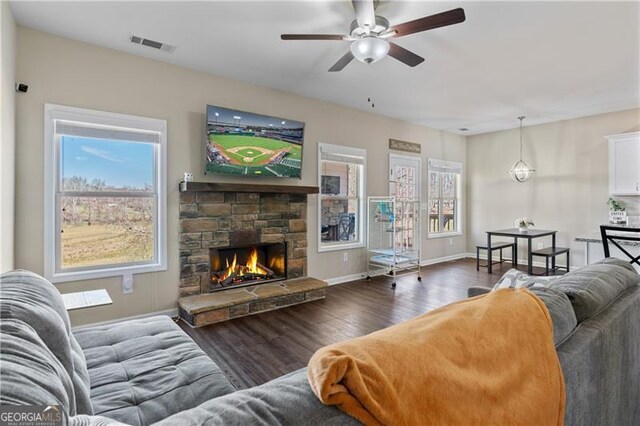 living area with visible vents, ceiling fan, a stone fireplace, wood finished floors, and baseboards