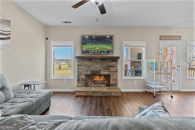 living room with a stone fireplace, wood finished floors, visible vents, and baseboards