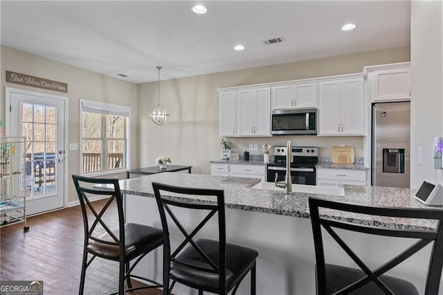 kitchen featuring stainless steel appliances, white cabinets, visible vents, and a breakfast bar area