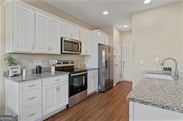 kitchen with appliances with stainless steel finishes, a sink, dark wood finished floors, and white cabinets