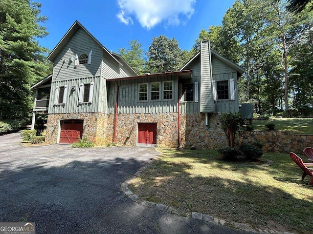 view of front of house with aphalt driveway, a garage, stone siding, board and batten siding, and a chimney