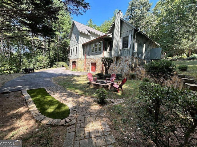 view of side of property with stone siding, an outdoor fire pit, a chimney, and driveway