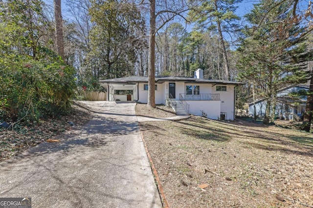 view of front of house with driveway, an attached carport, a chimney, and fence