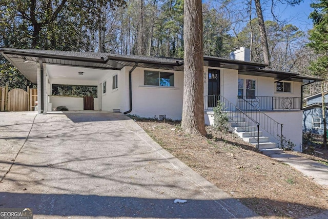 view of front of home featuring brick siding, a chimney, fence, an attached carport, and driveway