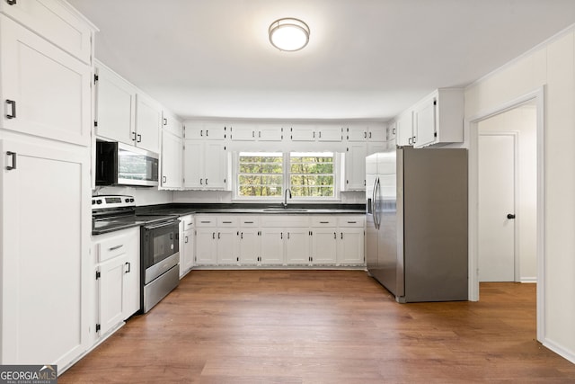 kitchen featuring appliances with stainless steel finishes, dark countertops, white cabinets, and a sink