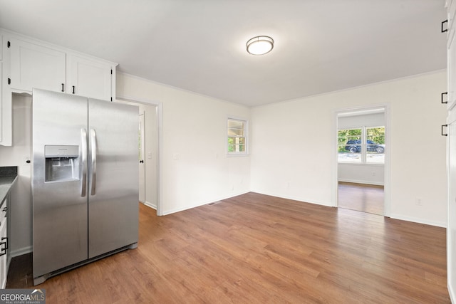 kitchen with light wood-type flooring, stainless steel fridge, baseboards, and white cabinets