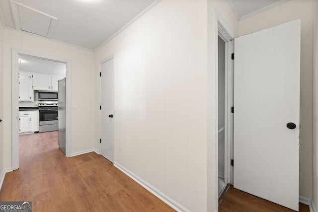 hallway with attic access, crown molding, and wood finished floors